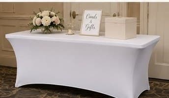 White tablecloth on a 6-foot table with a card box and floral at an indoor venue